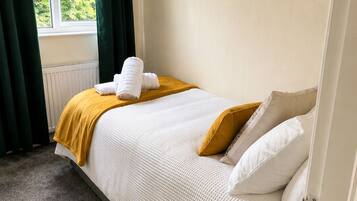 A bedroom with a bed, a window with curtains, a radiator, and a painting on the wall.