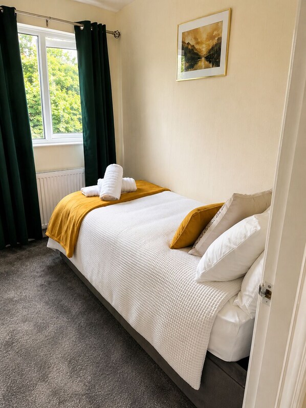 A bedroom with a bed, a window with curtains, a radiator, and a painting on the wall.
