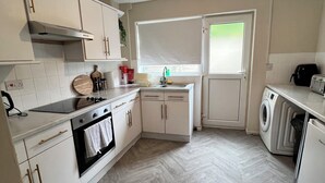 A modern kitchen with white cabinetry, a built-in oven, a washing machine, and a window with blinds. -  Stylish 3BR | Sleeps 5 | Long Stay welcome (Mansfield)