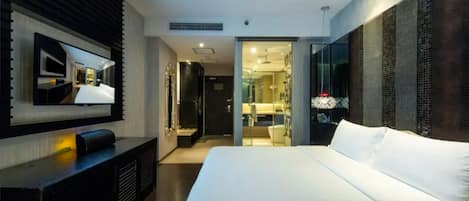 A modern hotel room with a large bed, a flat-screen TV mounted on the wall, and a walk-in closet.