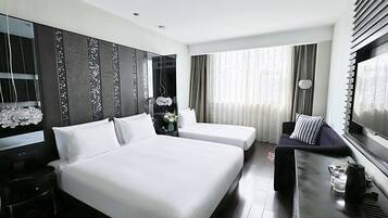 Habitación de hotel con dos camas, un sofá, un televisor y un escritorio con hervidor y vasos.