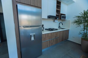 A modern kitchen with a stainless steel refrigerator, wooden cabinets, a microwave, and a sink.