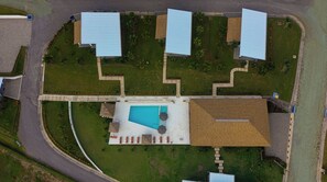 An aerial view of a property with a swimming pool, multiple buildings with blue roofs, and a well-maintained lawn.