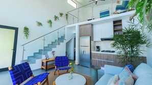 A modern interior with a staircase, seating area, kitchen, and a large plant.