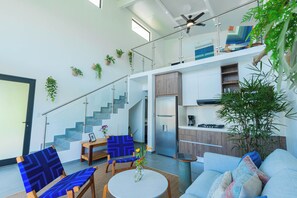 A modern interior with a staircase, seating area, kitchen, and a large plant.