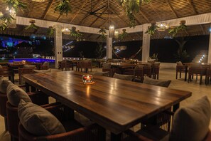 An outdoor dining area with wooden tables and chairs, hanging plants, and a thatched roof. - Pool, Yoga Studio -Private La Vibra Resort Villa 1 (Langostino)