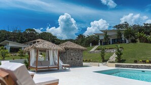 A poolside area with lounge chairs, a thatched-roof structure, and a stone wall.