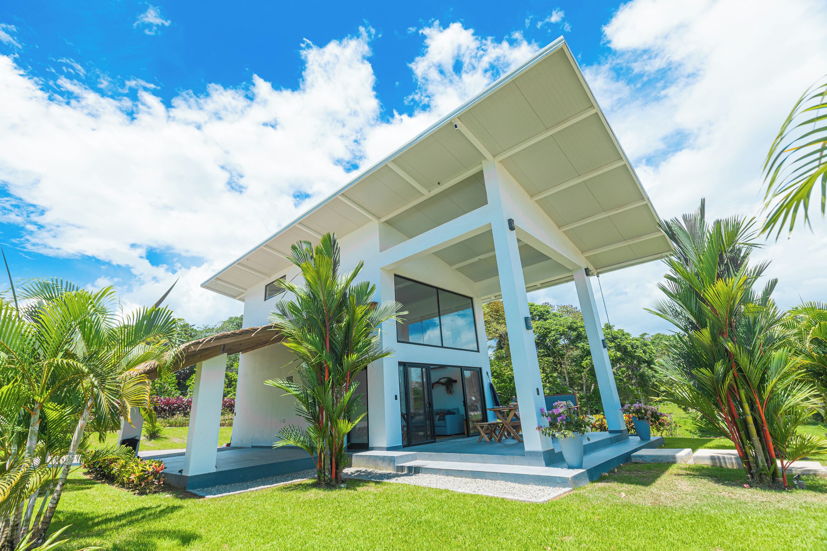 A modern house with a covered patio, large windows, and lush greenery.