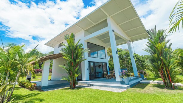 A modern house with a covered patio, large windows, and lush greenery.
