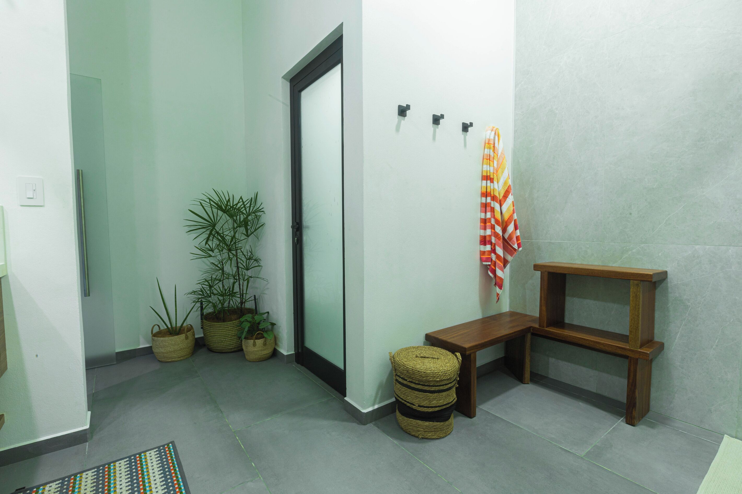 Un couloir avec une porte, des plantes en pot, un banc et une étagère fixée au mur.