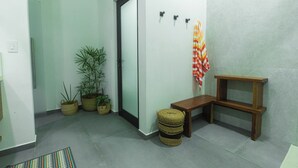 A hallway with a door, potted plants, a bench, and a wall-mounted shelf.