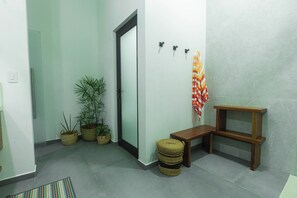 A hallway with a door, potted plants, a bench, and a wall-mounted shelf.