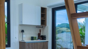 A modern kitchen with white cabinets, a wooden countertop, and a view of a tropical landscape through large sliding glass doors.