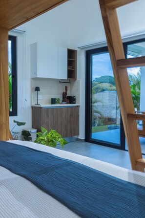 A modern kitchen with white cabinets, a wooden countertop, and a view of a tropical landscape through large sliding glass doors.