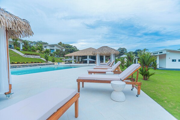 A poolside area with lounge chairs, a thatched-roof structure, and a pool.
