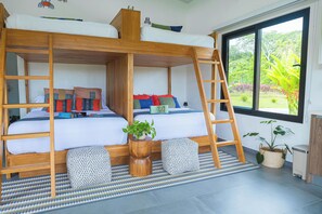 Een slaapkamer met een stapelbed, een klein tafeltje met een plant en een raam met uitzicht op groen.