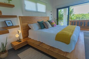 A bedroom with a wooden bed, bedside tables, a nightstand, a potted plant, and a view of the outdoors.