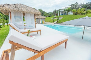 A poolside area with lounge chairs, a thatched-roof structure, and a clear view of the pool.