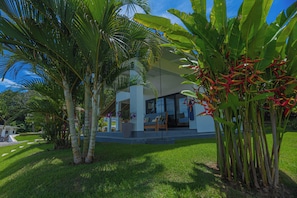 A modern house with a patio, surrounded by lush greenery and a clear blue sky.