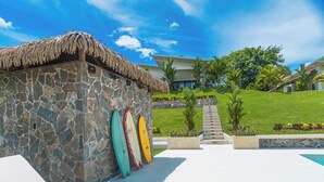 A stone building with a thatched roof, a pool area, and a view of a modern house in the background. - Pool, Yoga Studio -Private La Vibra Resort Villa 4 (Langostino)