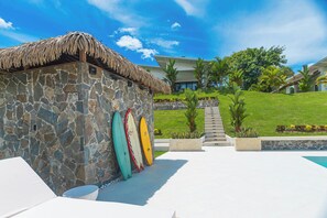 A stone building with a thatched roof, a pool area, and a view of a modern house in the background. - Pool, Yoga Studio -Private La Vibra Resort Villa 4 (Langostino)