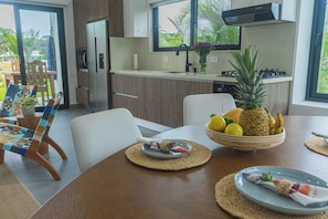 A modern kitchen with a dining area, a large window, and a fruit bowl on the table. - Pool, Yoga Studio -Private La Vibra Resort Villa 4 (Langostino)