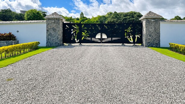 A gated entrance with a gravel driveway, stone walls, and a clear blue sky. - Pool, Yoga Studio -Private La Vibra Resort Villa 4 (Langostino)