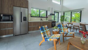 A modern kitchen with built-in appliances, a dining area with a table and chairs, and large windows offering a view of greenery. - Pool, Yoga Studio -Private La Vibra Resort Villa 4 (Langostino)