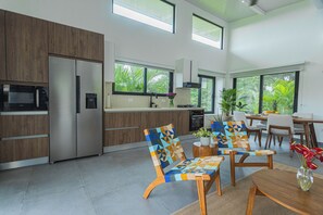 A modern kitchen with built-in appliances, a dining area with a table and chairs, and large windows offering a view of greenery. - Pool, Yoga Studio -Private La Vibra Resort Villa 4 (Langostino)