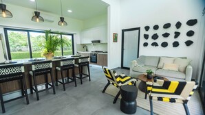 Une cuisine moderne avec des meubles blancs, un coin repas avec des chaises à motifs et un salon agrémenté d’un canapé et d’œuvres d’art décoratives.