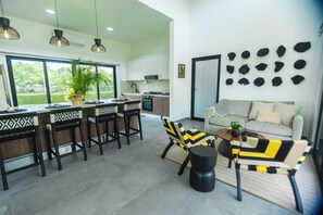 A modern kitchen with white cabinets, a dining area with patterned chairs, and a living room with a sofa and decorative wall art. - Pool, Yoga Studio -La Vibra Private Resort Villa 5 (Langostino)