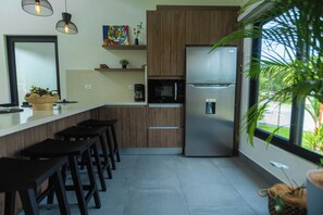 A modern kitchen with wooden cabinets, a stainless steel refrigerator, a microwave, and a large window. - Pool, Yoga Studio -La Vibra Private Resort Villa 5 (Langostino)