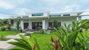 Une maison moderne à deux étages dotée d’un patio couvert, d’un espace salon extérieur et d’un jardin luxuriant.