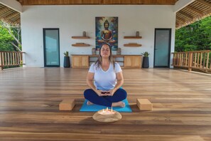 Una persona medita su un pavimento di legno, con una candela davanti, circondata da panche in legno e un dipinto del Buddha sulla parete.