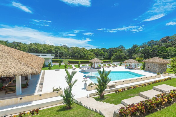 Een resort met een zwembad, loungegedeeltes en constructies met rieten daken.