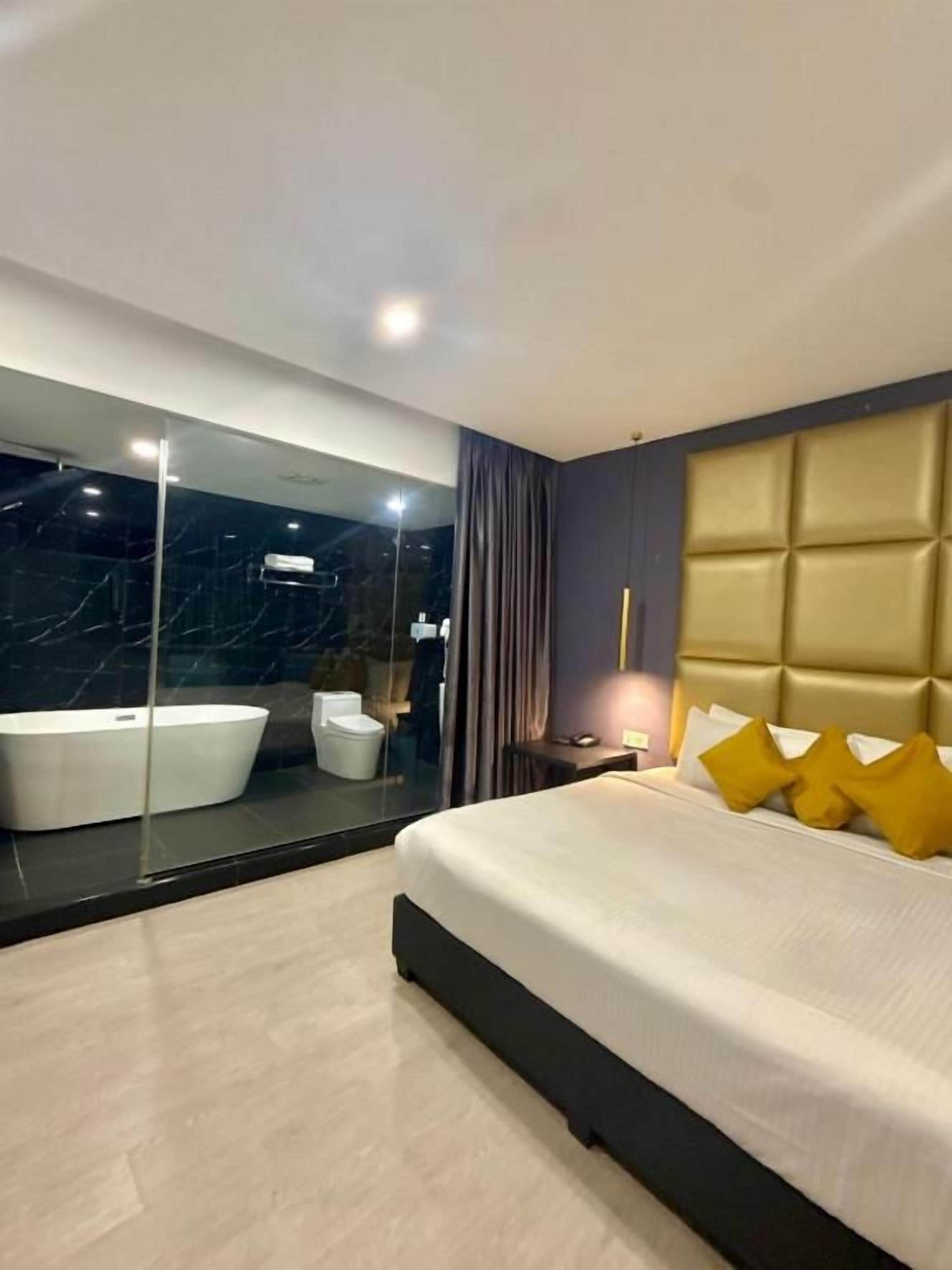 Une chambre à coucher moderne avec un grand lit, une salle de bain fermée par des parois de verre et une zone de douche carrelée en marbre.