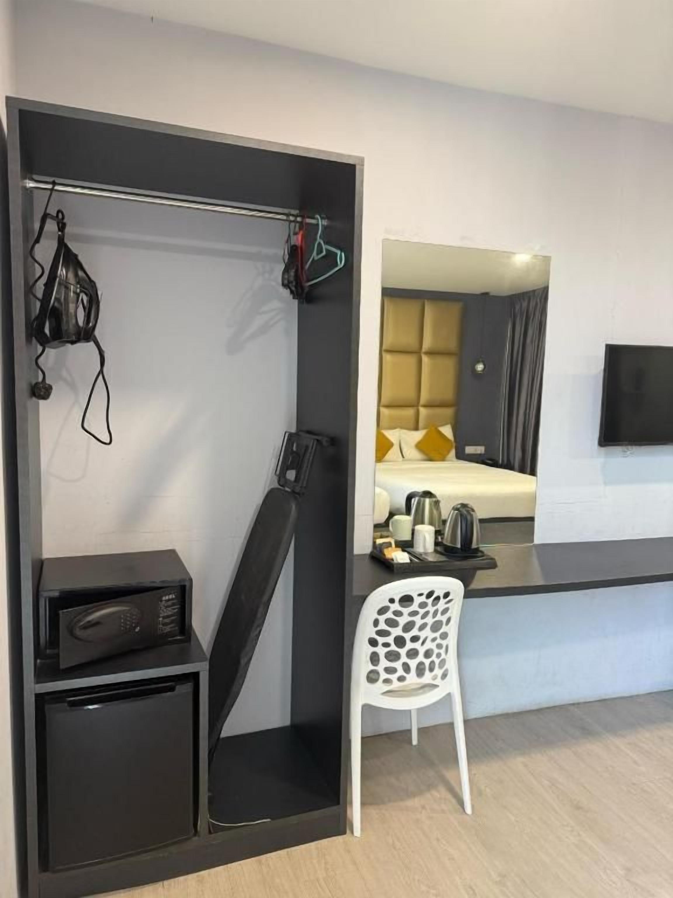 A hotel room with a bed, a TV, a desk with a chair, and a coat rack with clothes.