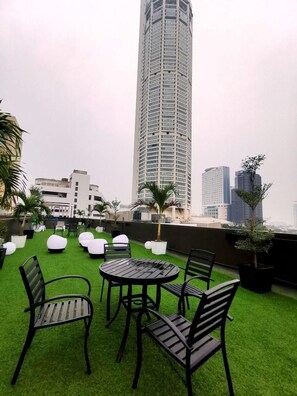 A rooftop terrace with artificial grass, seating, and a view of a tall building. - The Wow Boutique (George Town)