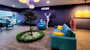 A modern interior with a round green carpet, blue sofas, and a tree centerpiece. - The Wow Boutique (George Town)
