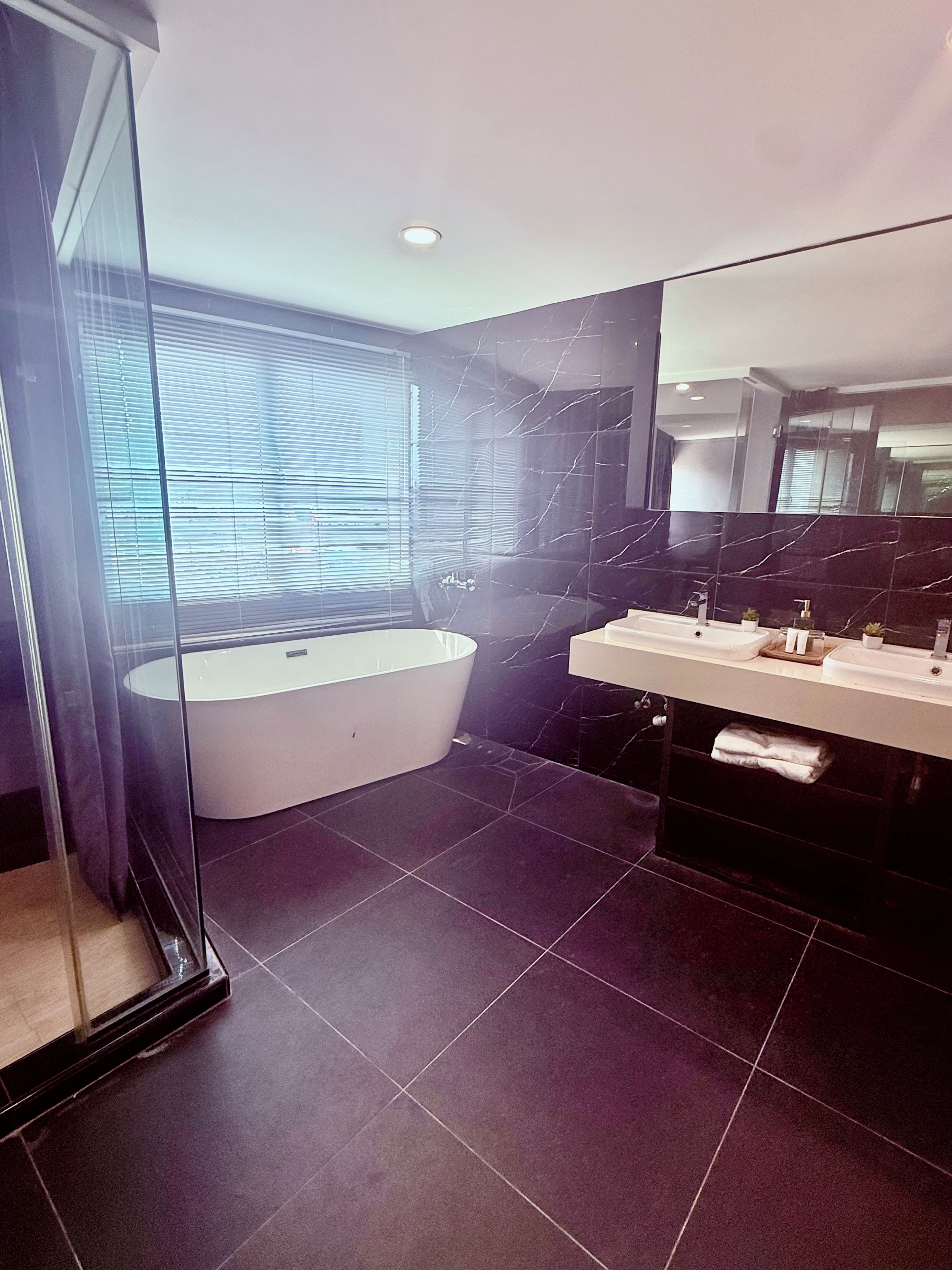Un baño moderno con una bañera independiente, un tocador con espejo y suelo de baldosas oscuras.