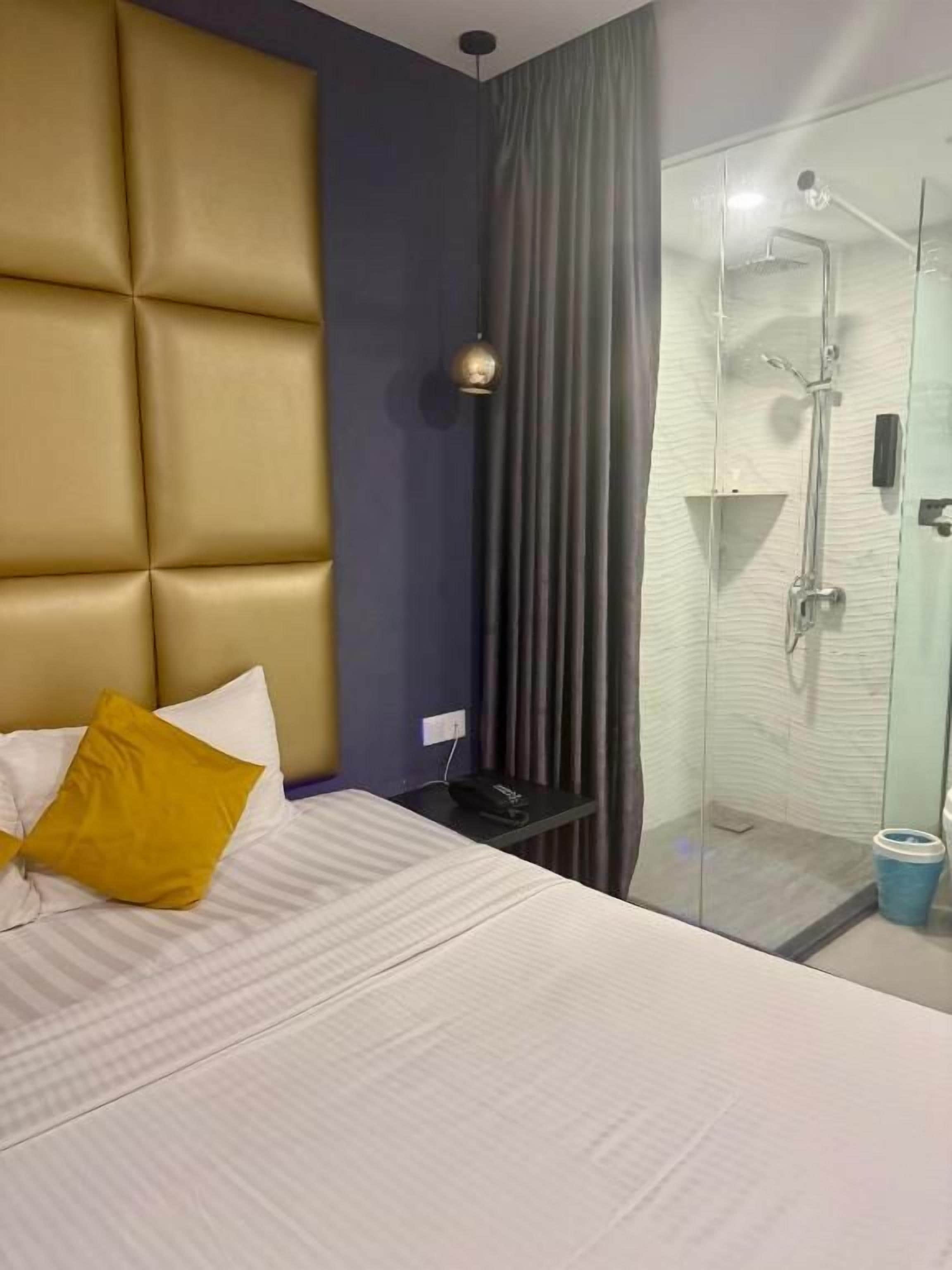 Quarto de hotel com cama, box de chuveiro e mesa de cabeceira.