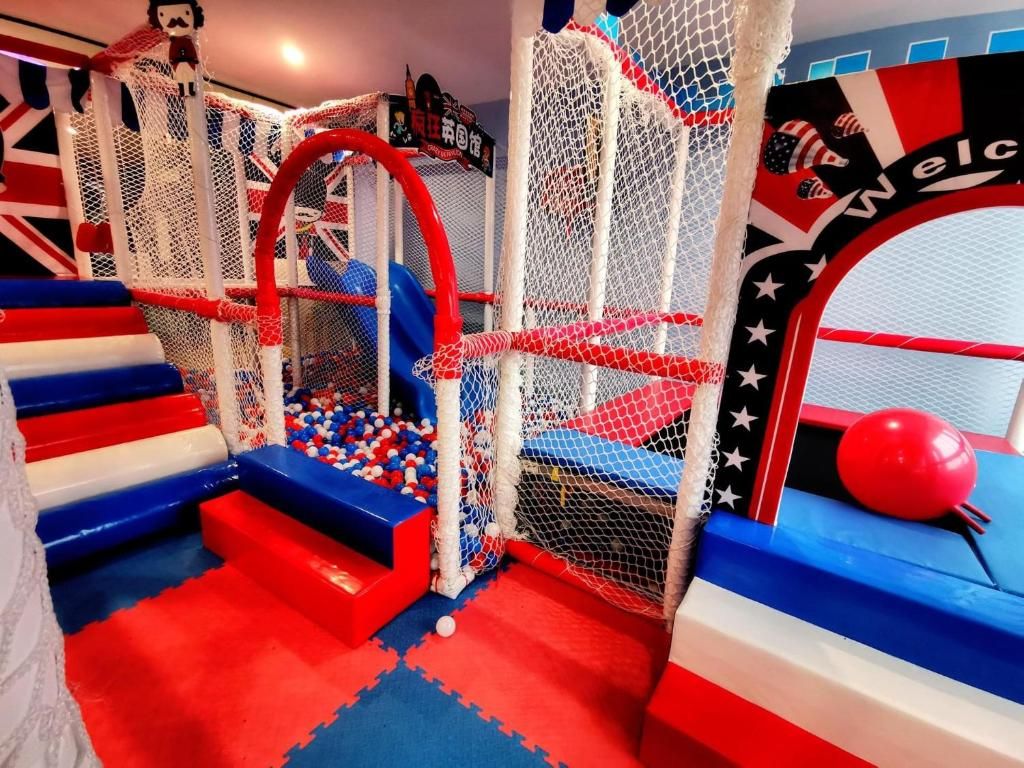 Un área de juegos con una estructura de escalada con red, escalones acolchados y una piscina de pelotas.