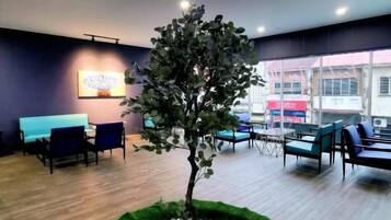 Un interior moderno con un árbol central rodeado por una disposición circular de piedras, una zona de estar con sillas e iluminación en el techo con forma de nubes.