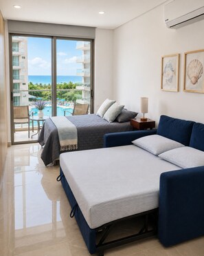 Ein Hotelzimmer mit einem Bett, einem Sofa, einem kleinen Tisch und einer Lampe. Es gibt ein Fenster mit Blick auf einen Pool und ein Gebäude.
