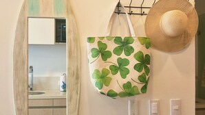 A wall-mounted surfboard-shaped mirror, a clover-patterned tote bag, and a straw hat hanging on hooks. - Suite Apartment | Ocean View | Infinity Pool | Rooftop | Jacuzzi (Santa Marta)