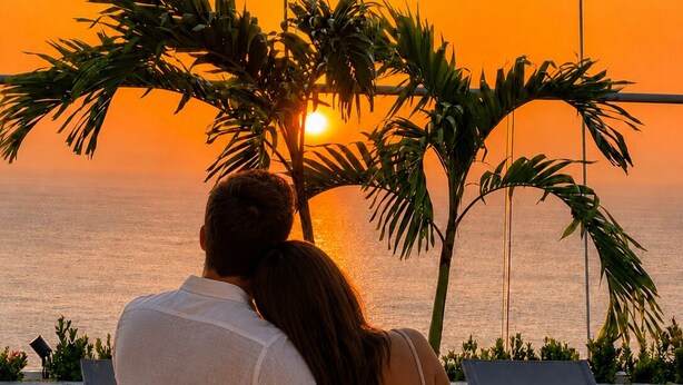 A couple sitting by a poolside during sunset, overlooking the ocean. - Suite Apartment | Ocean View | Infinity Pool | Rooftop | Jacuzzi (Santa Marta)