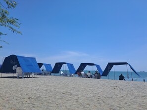 Ein Strand mit mehreren blauen Zelten und weißen Stühlen.
