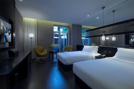 A hotel room with two beds, a desk, a chair, a mirror, and a window with a view of the outside.