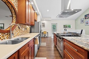 A modern kitchen with wooden cabinets, a large island, stainless steel appliances, and a tiled backsplash. - Family Friendly, Pizza Oven & BBQ, Near Downtown (St. Augustine)