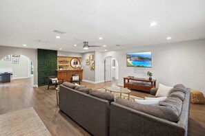 A spacious living area with a large gray sectional sofa, a coffee table, and a television mounted on the wall. - Family Friendly, Pizza Oven & BBQ, Near Downtown (St. Augustine)